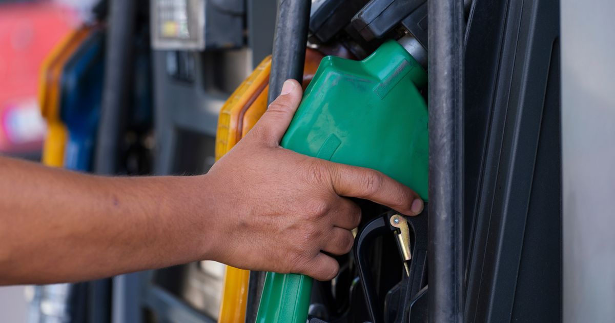 Close-up of a hand gripping a green fuel nozzle at a fuel pump